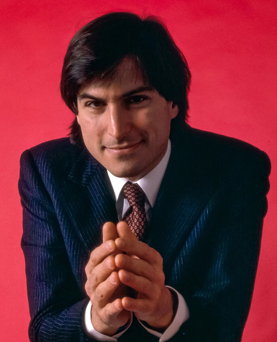 Portrait of Steve Jobs seated against a red background in January 1984